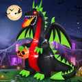 Black dragon inflatable with green wings breathing fire and holding a jack-o'-lantern at night