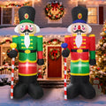 Two nutcracker soldier inflatables in green and red coats holding candy canes by a front door