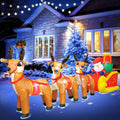 Santa in a gold and red sleigh pulled by three reindeer inflatable in front of a blue-lit house at night