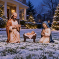Painted metal nativity figures of Joseph, Mary kneeling and the baby in a manger in the snow